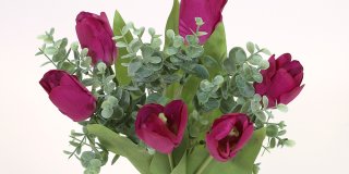 En närbild på en bukett med konstgjorda lila tulpaner och gröna blad, blandade med små gröna kvistar av eukalyptusliknande blad.